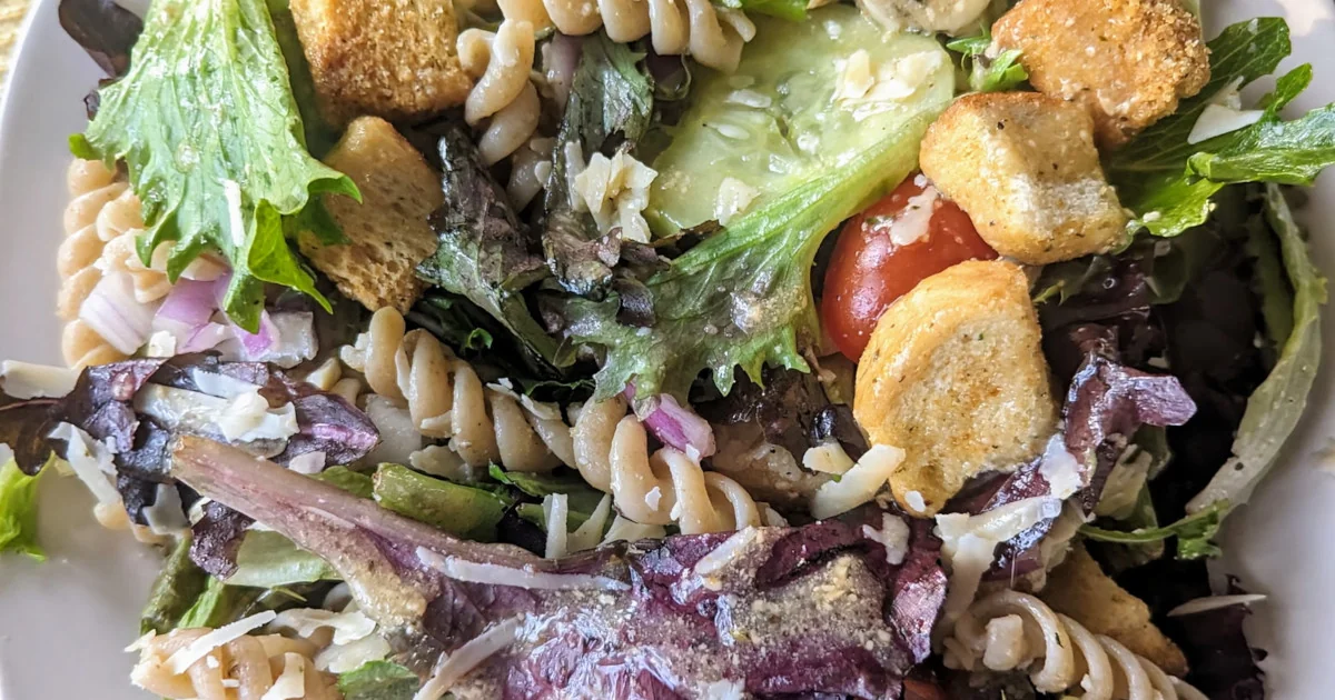 A colorul chicken ceasar salad with pasta, lettuce, tomatoes, croutons, and parmesan cheese in a white bowl.